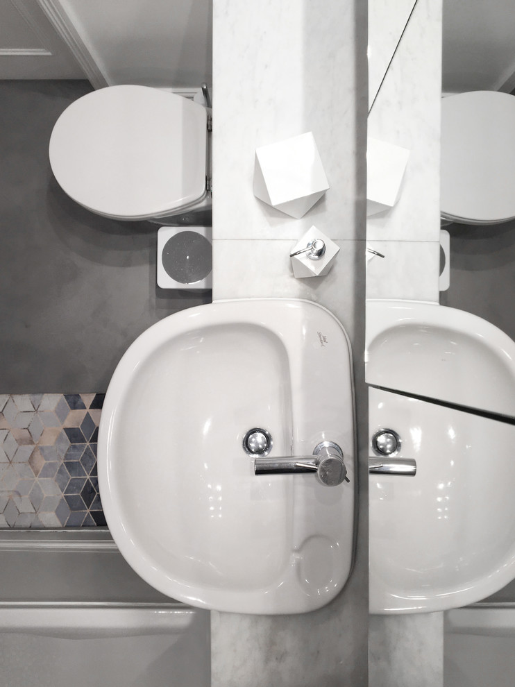 ロンドンにあるお手頃価格の小さなコンテンポラリースタイルのおしゃれなマスターバスルーム (ガラス扉のキャビネット、白いキャビネット、ドロップイン型浴槽、シャワー付き浴槽	、壁掛け式トイレ、グレーのタイル、白い壁、コンクリートの床、オーバーカウンターシンク、大理石の洗面台、グレーの床、開き戸のシャワー) の写真