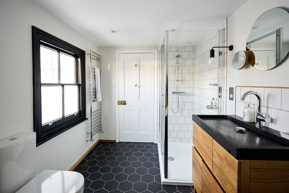 This is an example of a medium sized scandinavian family bathroom in Sussex with flat-panel cabinets, light wood cabinets, a claw-foot bath, a corner shower, a one-piece toilet, white tiles, ceramic tiles, white walls, ceramic flooring, an integrated sink, solid surface worktops, black floors and a hinged door.