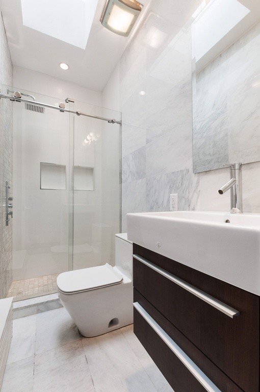 Corner shower - small modern master white tile and porcelain tile marble floor and white floor corner shower idea in New York with flat-panel cabinets, distressed cabinets, a one-piece toilet, gray walls, a vessel sink and a hinged shower door