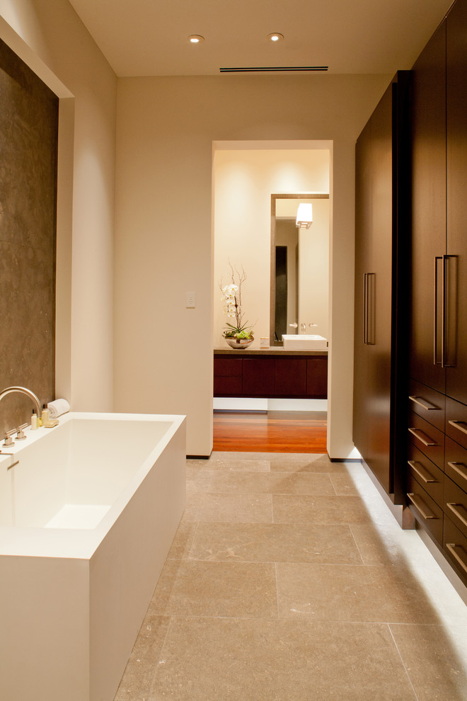 Modelo de cuarto de baño largo y estrecho actual con lavabo sobreencimera, armarios con paneles lisos, puertas de armario de madera en tonos medios, bañera exenta y paredes blancas