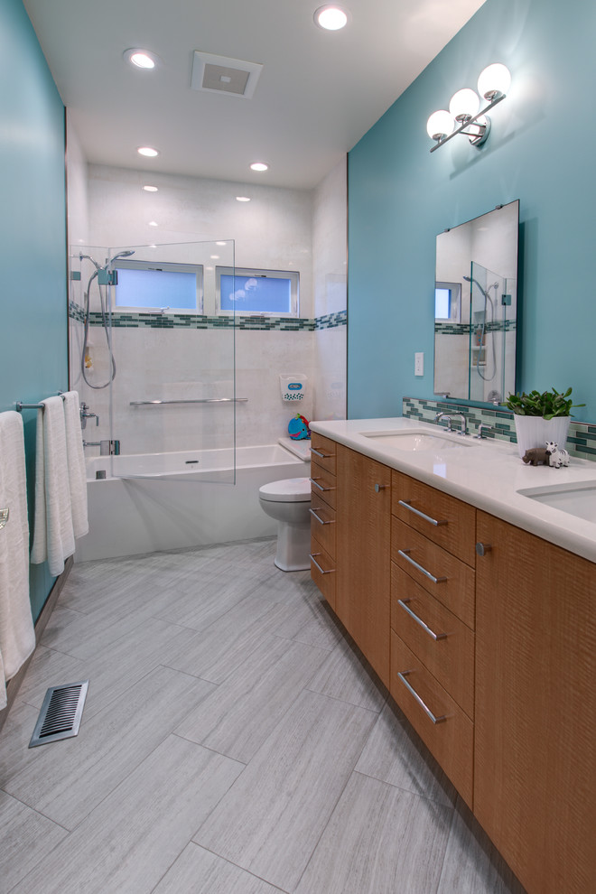 Inspiration pour une salle de bain design en bois clair de taille moyenne pour enfant avec un placard à porte plane, une baignoire en alcôve, un combiné douche/baignoire, WC à poser, un carrelage blanc, des carreaux de porcelaine, un mur bleu, un sol en carrelage de porcelaine, un lavabo encastré, un plan de toilette en quartz modifié, une cabine de douche à porte battante, un plan de toilette blanc, une niche, un banc de douche et meuble-lavabo suspendu.