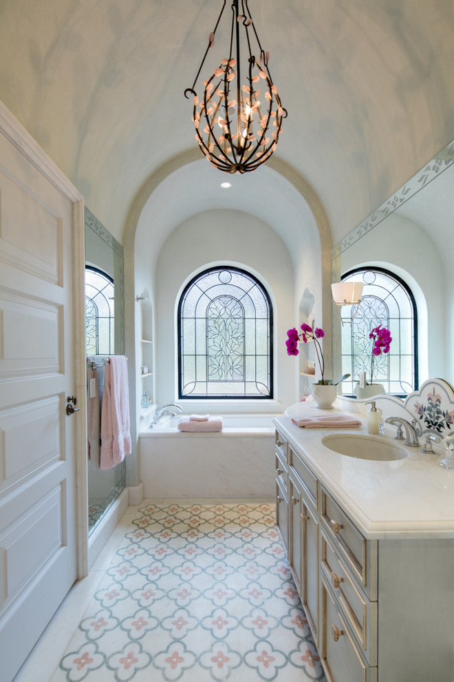 Réalisation d'une douche en alcôve méditerranéenne avec des portes de placard grises, une baignoire encastrée, un carrelage beige, un carrelage rose, un sol multicolore et une cabine de douche à porte battante.