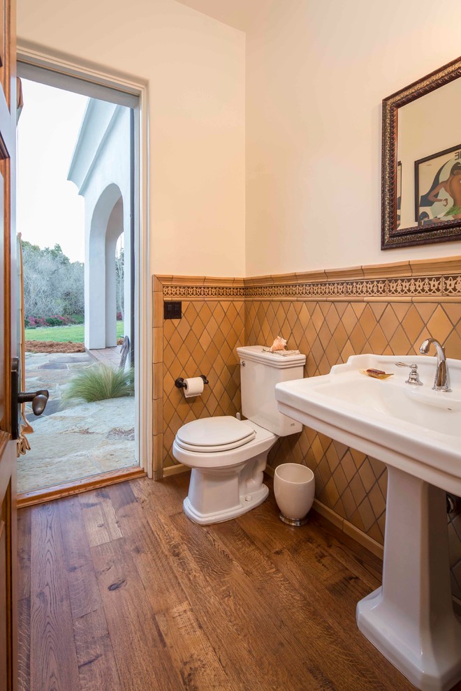 Medelhavsstil inredning av ett stort badrum med dusch, med en toalettstol med separat cisternkåpa, porslinskakel, vita väggar, mellanmörkt trägolv och ett piedestal handfat
