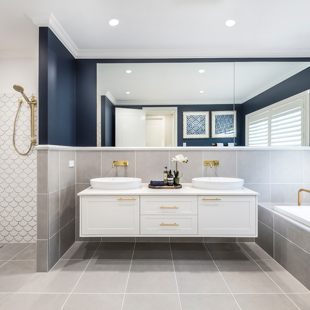 This is an example of a nautical ensuite bathroom in Brisbane with shaker cabinets, white cabinets, a built-in bath, grey tiles, blue walls, a vessel sink, grey floors and white worktops.