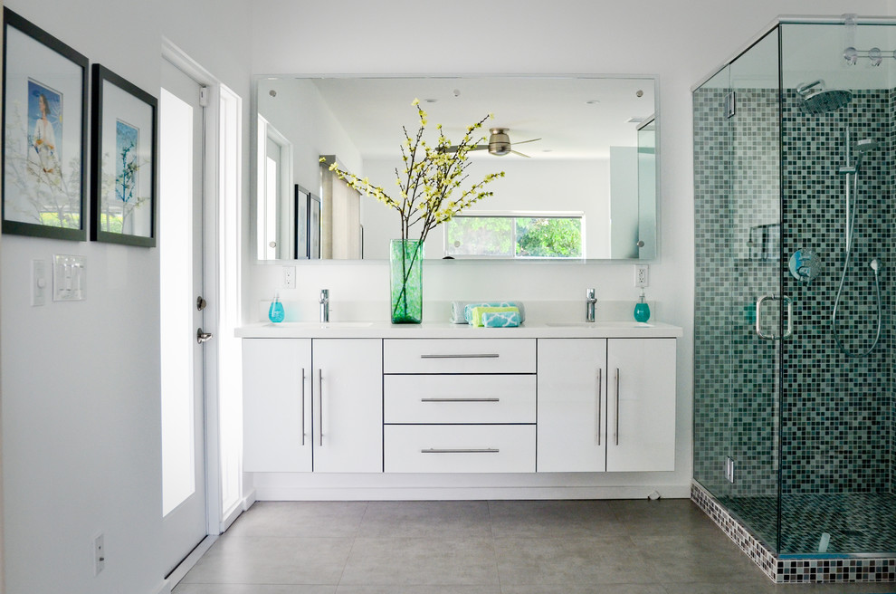 Пример оригинального дизайна: большая ванная комната в современном стиле с врезной раковиной, плоскими фасадами, белыми фасадами, столешницей из искусственного кварца, угловым душем, разноцветной плиткой, плиткой мозаикой, белыми стенами, полом из керамогранита, душевой кабиной и белой столешницей