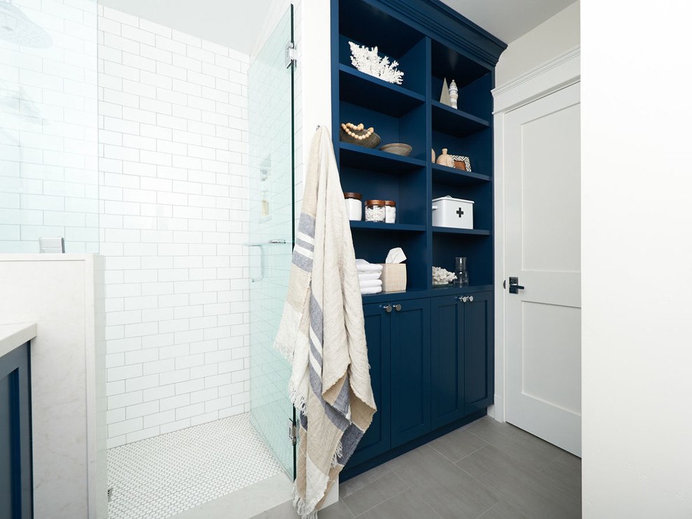 Example of a mid-sized beach style white tile and ceramic tile ceramic tile and gray floor corner shower design in San Diego with shaker cabinets, white cabinets, blue walls, an undermount sink, quartz countertops, a hinged shower door and white countertops