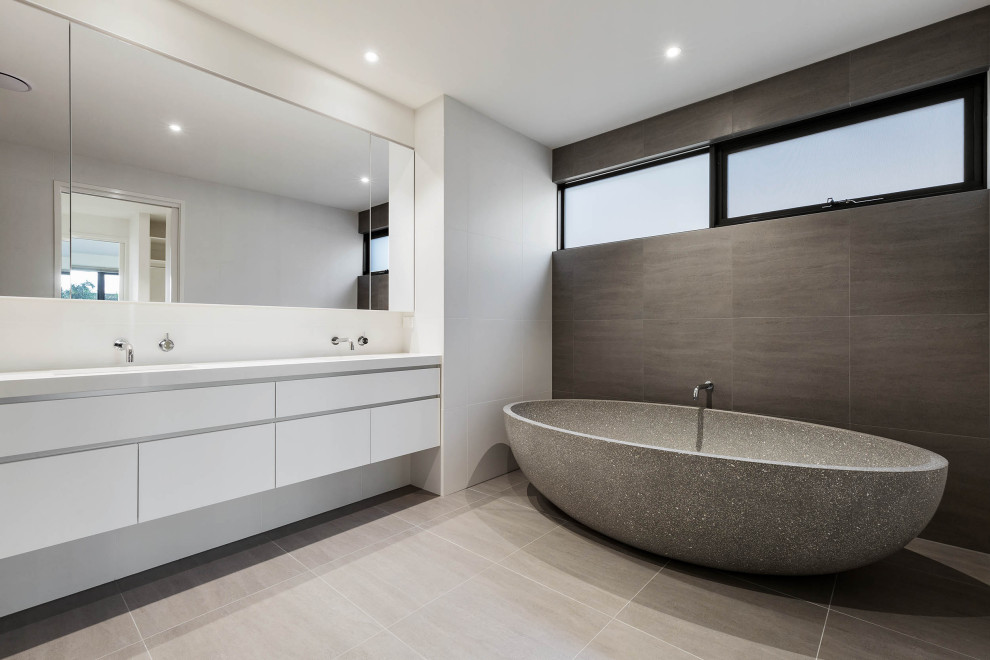 Exemple d'une salle de bain moderne avec un placard à porte plane, des portes de placard blanches, une baignoire indépendante, un carrelage gris, un mur blanc, un sol gris, un plan de toilette blanc, meuble double vasque et meuble-lavabo suspendu.