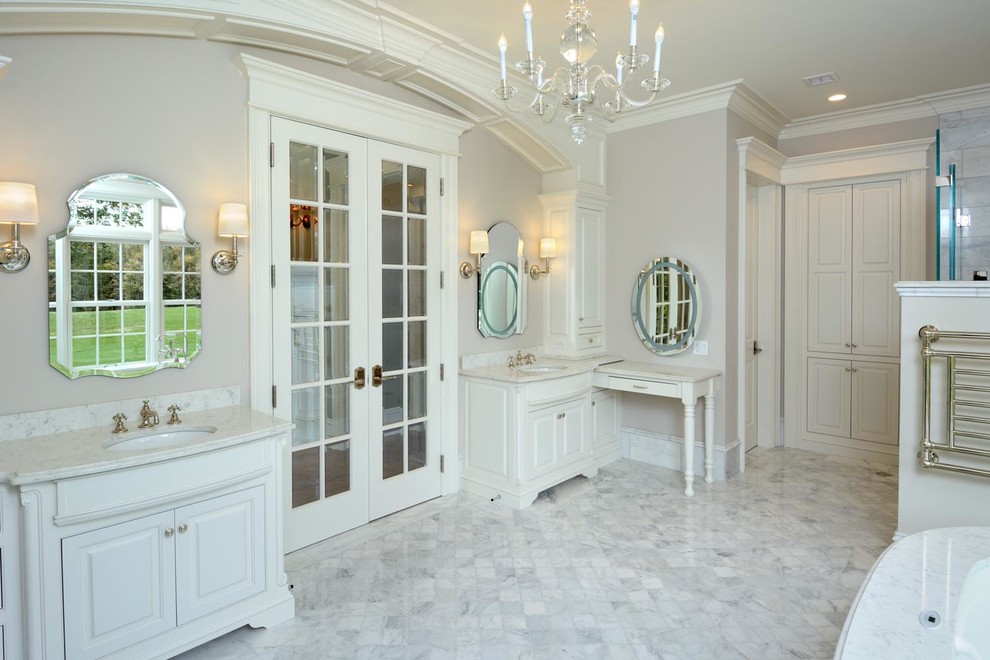 На фото: большая главная ванная комната в стиле неоклассика (современная классика) с врезной раковиной, фасадами с выступающей филенкой, белыми фасадами, белой плиткой, бежевыми стенами и мраморным полом с