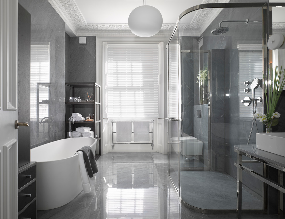 ロンドンにある広いコンテンポラリースタイルのおしゃれなマスターバスルーム (大理石の洗面台、置き型浴槽、壁掛け式トイレ、グレーのタイル、大理石の床、オープンシェルフ) の写真