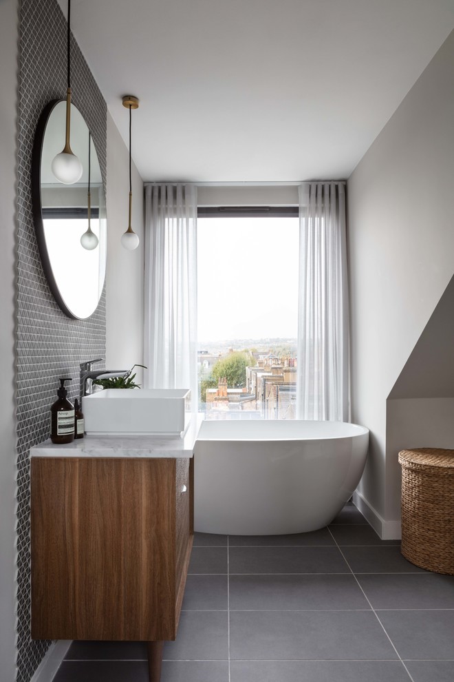 This is an example of a medium sized contemporary family bathroom in London with flat-panel cabinets, medium wood cabinets, a freestanding bath, grey tiles, ceramic tiles, grey walls, ceramic flooring, a console sink, marble worktops, grey floors and white worktops.