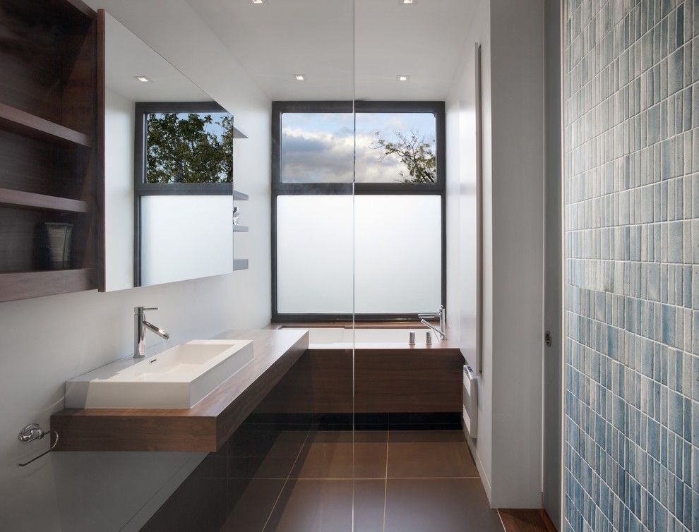 Photo of a modern half tiled bathroom in Montreal with a vessel sink, wooden worktops, an alcove bath, blue tiles and open cabinets.