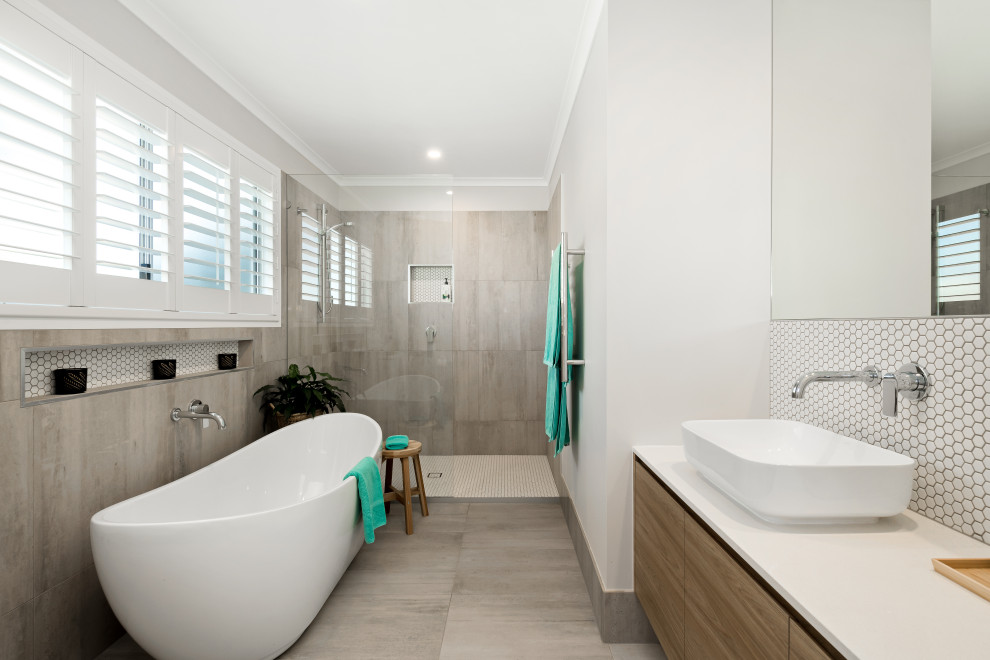 Exempel på ett mellanstort maritimt vit vitt badrum, med skåp i mellenmörkt trä, ett fristående badkar, en öppen dusch, en toalettstol med hel cisternkåpa, grå kakel, porslinskakel, grå väggar, klinkergolv i porslin, ett fristående handfat, bänkskiva i kvarts, grått golv, med dusch som är öppen och släta luckor
