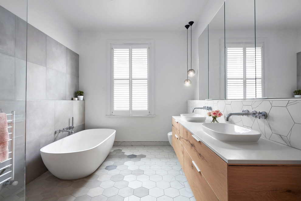 Bild på ett stort funkis en-suite badrum, med släta luckor, skåp i ljust trä, ett fristående badkar, grå kakel, vit kakel, vita väggar, ett fristående handfat, en öppen dusch, mosaik, mosaikgolv och bänkskiva i akrylsten
