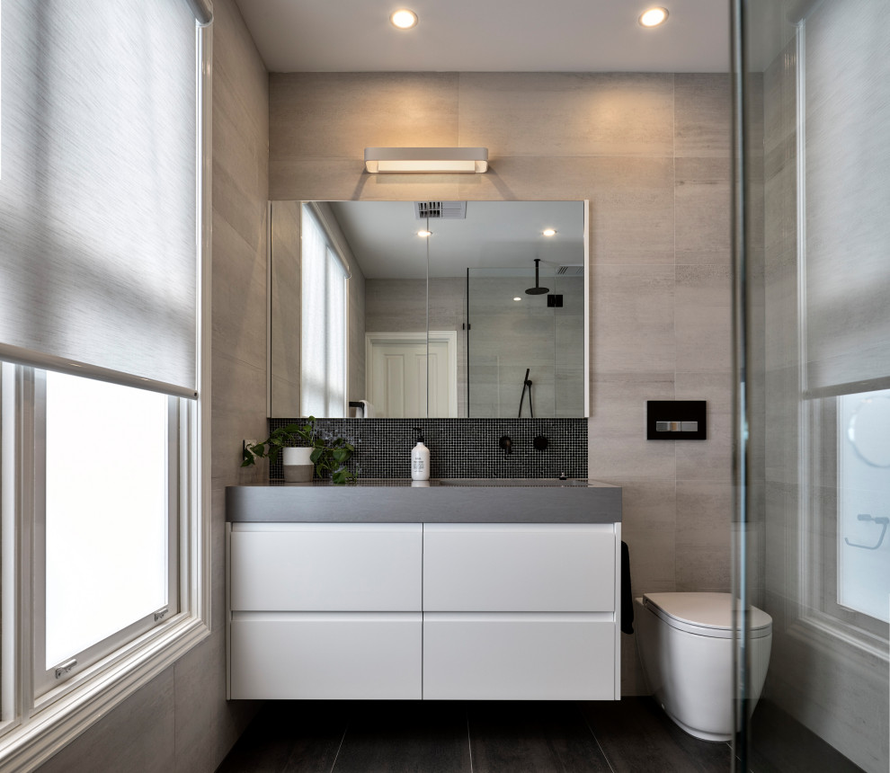 Inspiration för ett mellanstort funkis grå grått badrum med dusch, med vita skåp, en vägghängd toalettstol, grå kakel, porslinskakel, ett integrerad handfat och svart golv