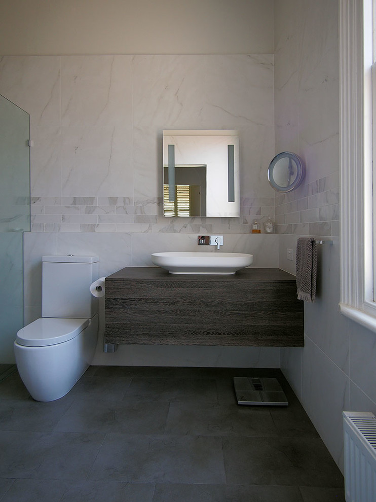 Inspiration för mellanstora moderna en-suite badrum, med luckor med upphöjd panel, skåp i mörkt trä, en öppen dusch, en toalettstol med hel cisternkåpa, grå kakel, stenkakel, grå väggar, klinkergolv i porslin, ett fristående handfat och träbänkskiva