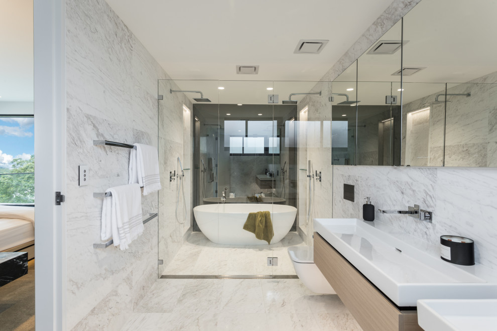 Modern inredning av ett badrum, med släta luckor, skåp i ljust trä, ett fristående badkar, våtrum, vit kakel, ett konsol handfat, vitt golv och dusch med gångjärnsdörr