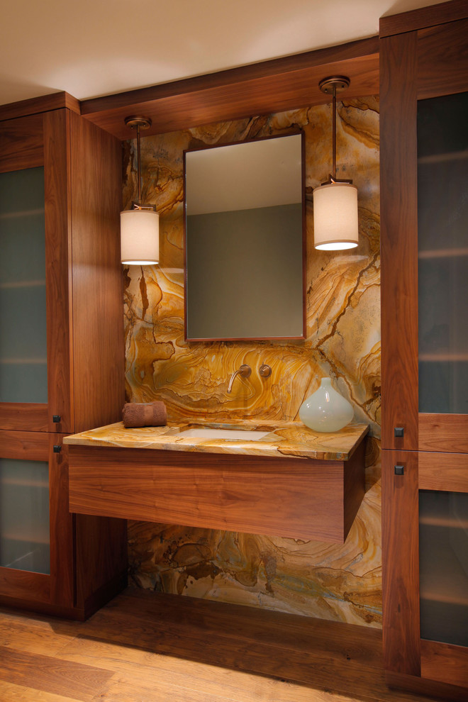 Bild på ett funkis badrum, med ett undermonterad handfat, skåp i mellenmörkt trä, brun kakel, stenhäll, mellanmörkt trägolv och släta luckor
