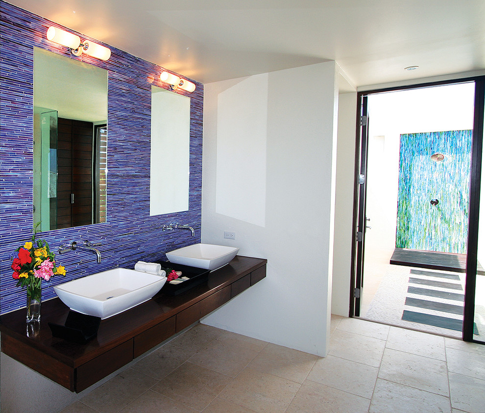 Photo of a medium sized world-inspired ensuite bathroom in New York with a vessel sink, flat-panel cabinets, dark wood cabinets, wooden worktops, a double shower, a one-piece toilet, blue tiles, mosaic tiles, white walls and ceramic flooring.