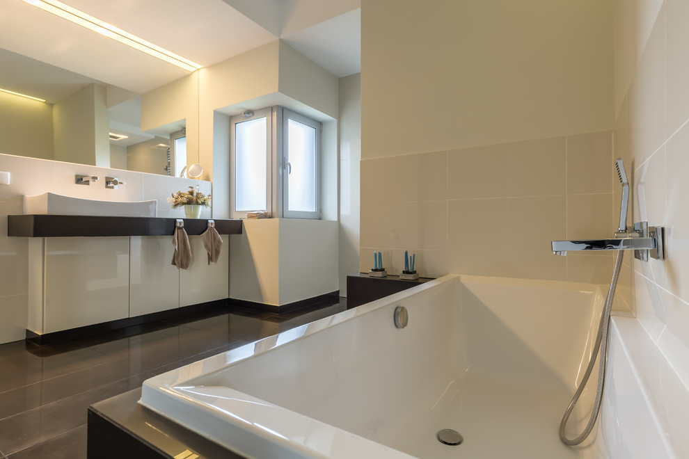 This is an example of a medium sized contemporary ensuite bathroom in Los Angeles with flat-panel cabinets, white cabinets, a corner bath, beige tiles, ceramic tiles, beige walls, slate flooring, a vessel sink and grey floors.