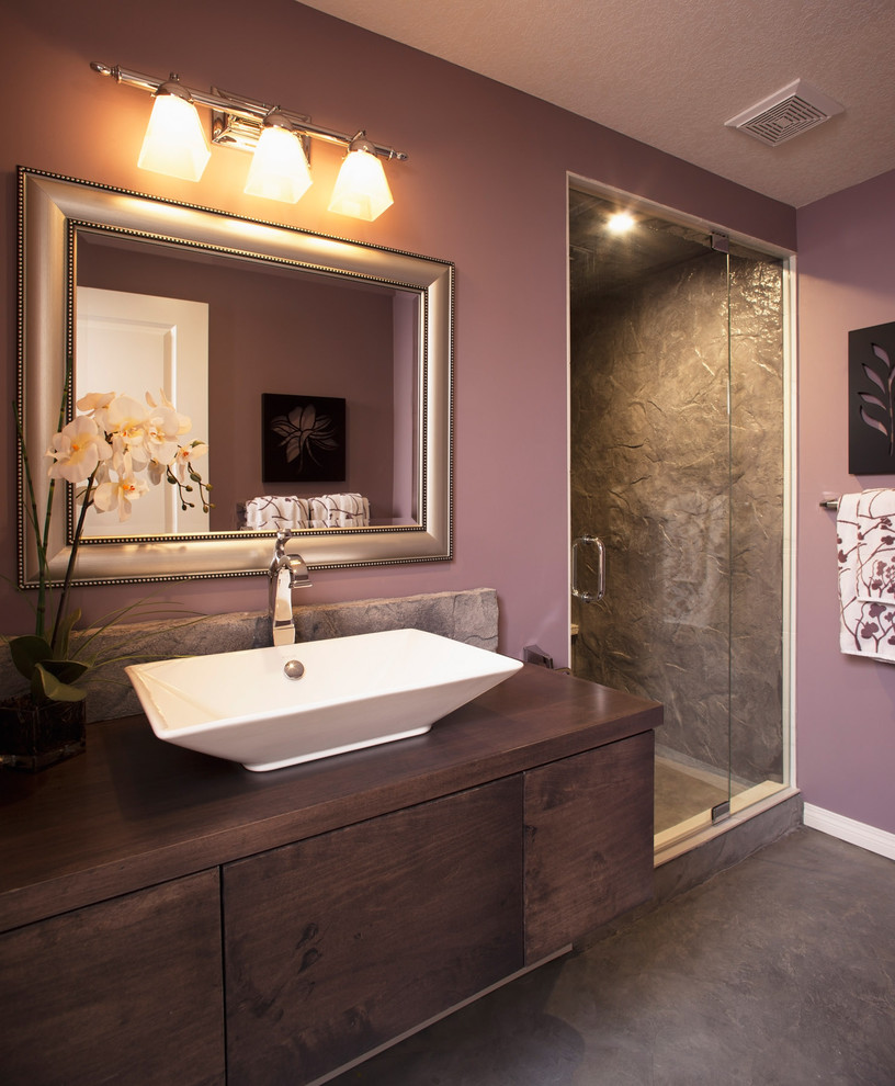 Photo of a medium sized contemporary ensuite bathroom in Calgary with flat-panel cabinets, dark wood cabinets, an alcove shower, brown tiles, stone tiles, purple walls, ceramic flooring, a vessel sink, wooden worktops, brown floors and a hinged door.