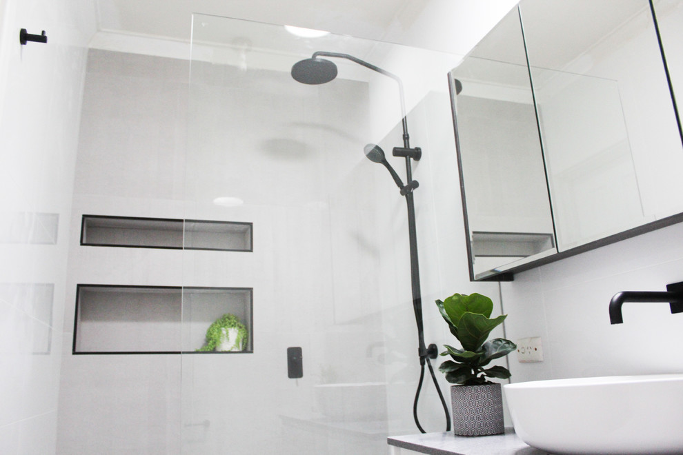 Inredning av ett modernt litet grå grått badrum med dusch, med släta luckor, vita skåp, en öppen dusch, en toalettstol med hel cisternkåpa, grå kakel, porslinskakel, grå väggar, klinkergolv i porslin, ett fristående handfat, bänkskiva i akrylsten, grått golv och med dusch som är öppen