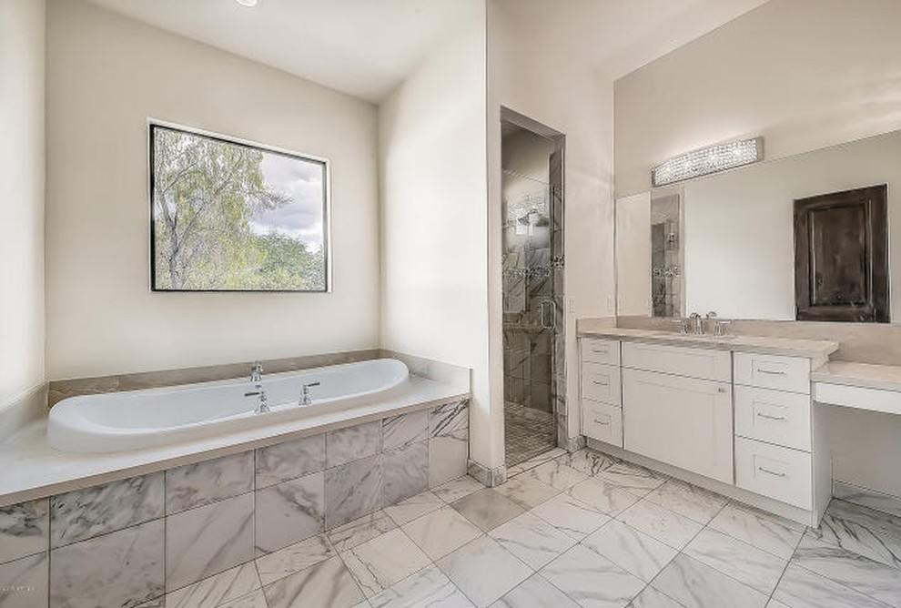 Inspiration for a large mediterranean ensuite bathroom in Phoenix with raised-panel cabinets, white cabinets, a built-in bath, an alcove shower, a two-piece toilet, beige tiles, marble tiles, white walls, marble flooring, a submerged sink, marble worktops, white floors, a hinged door and beige worktops.