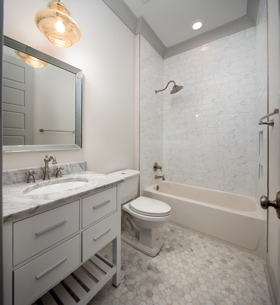 Bild på ett mellanstort vintage badrum med dusch, med släta luckor, vita skåp, ett badkar i en alkov, en dusch/badkar-kombination, en toalettstol med hel cisternkåpa, grå kakel, vit kakel, porslinskakel, grå väggar, mosaikgolv, ett undermonterad handfat och marmorbänkskiva