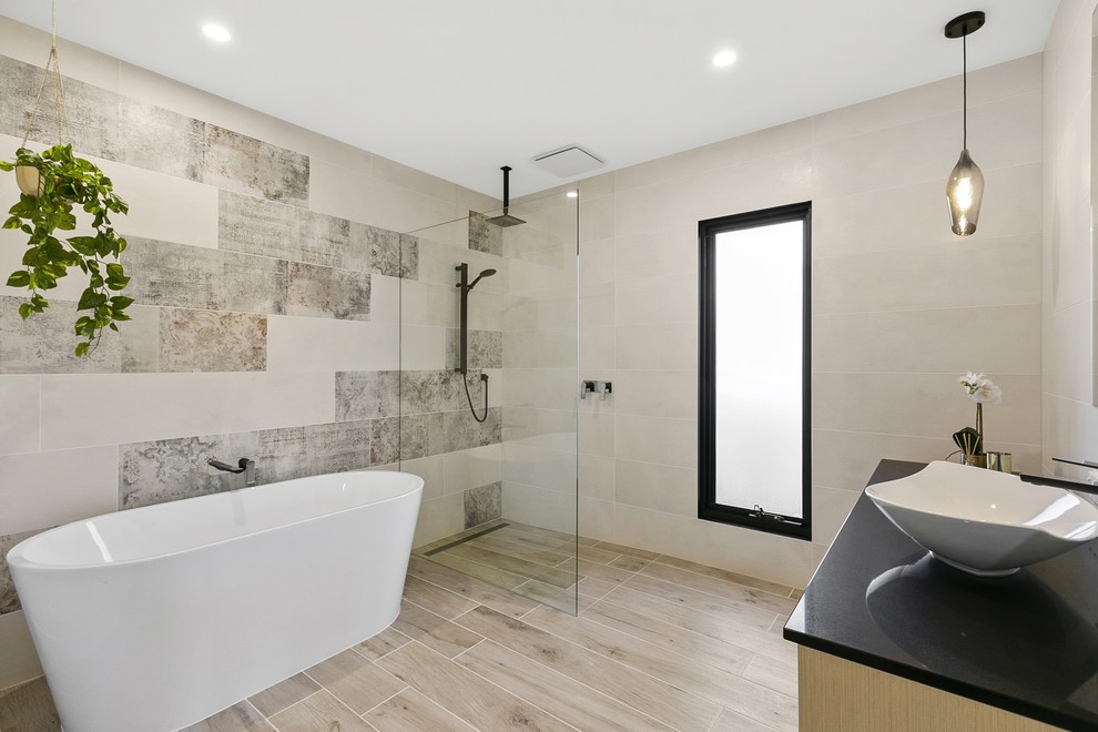 На фото: ванная комната в современном стиле с бежевыми фасадами, отдельно стоящей ванной, душевой комнатой, бежевой плиткой, бежевыми стенами, настольной раковиной, бежевым полом, открытым душем и черной столешницей с
