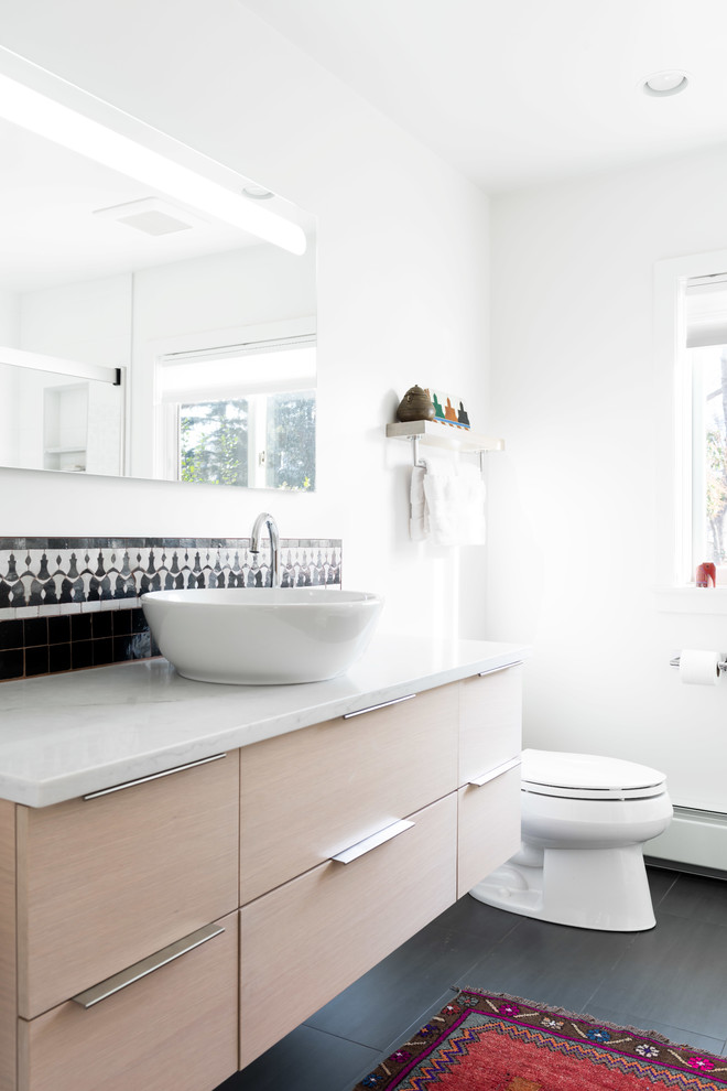 Inspiration pour une salle de bain design en bois clair avec un placard à porte plane, un carrelage noir et blanc, un mur blanc, une vasque, un sol noir et un plan de toilette blanc.