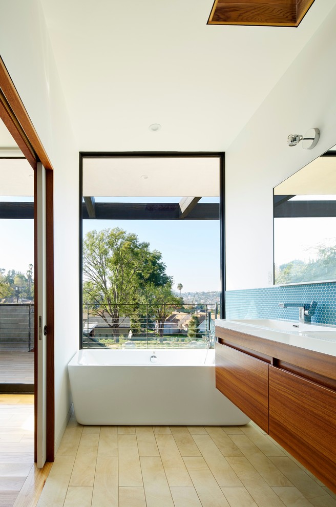 Modernes Badezimmer mit flächenbündigen Schrankfronten, hellbraunen Holzschränken, freistehender Badewanne, blauen Fliesen, Mosaikfliesen und weißer Wandfarbe in Los Angeles