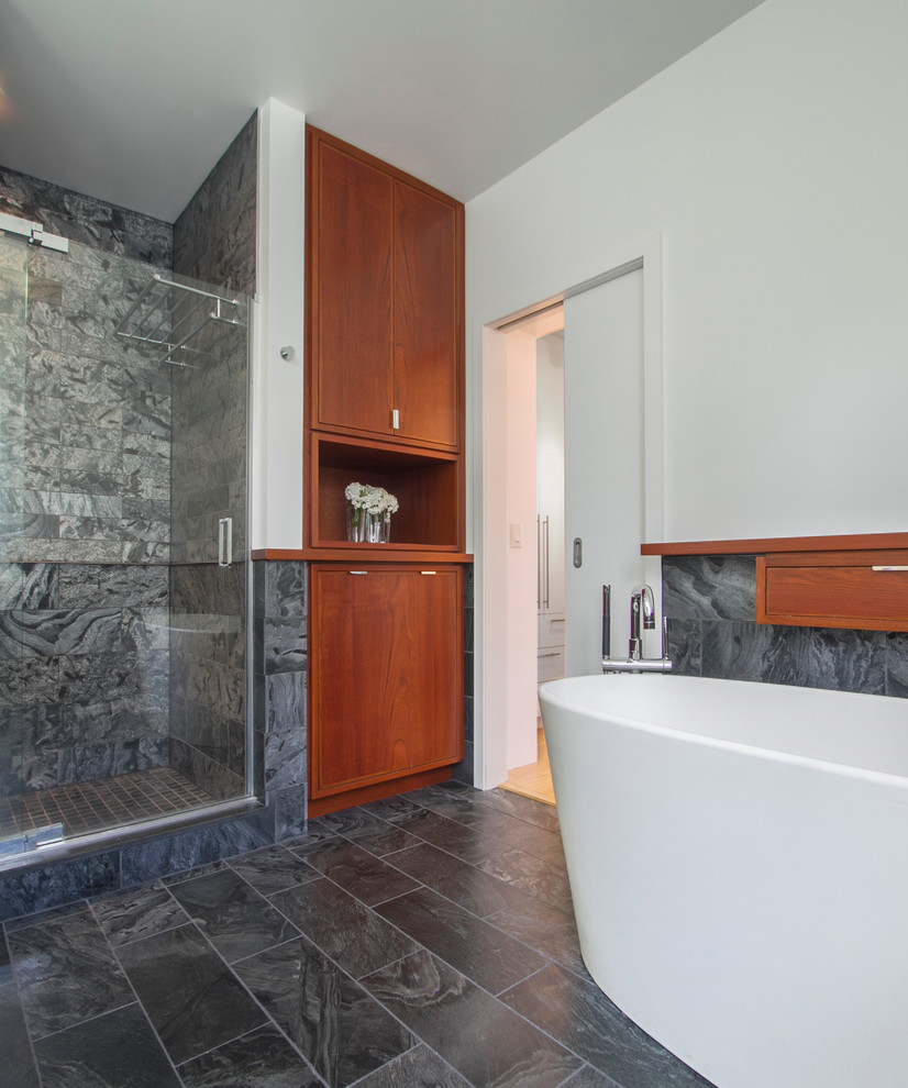 Trendy master gray tile and ceramic tile ceramic tile bathroom photo in New York with an undermount sink, flat-panel cabinets, medium tone wood cabinets, solid surface countertops, a two-piece toilet and white walls