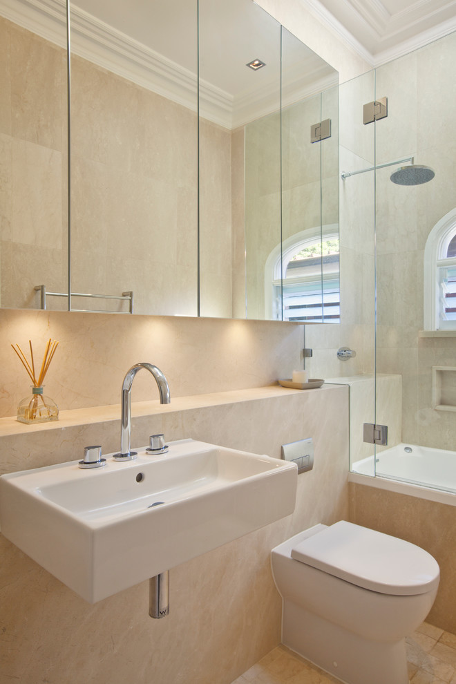 Inspiration for a large classic family bathroom in Sydney with a wall-mounted sink, flat-panel cabinets, a built-in bath, a shower/bath combination, a wall mounted toilet, beige tiles, stone tiles and white walls.