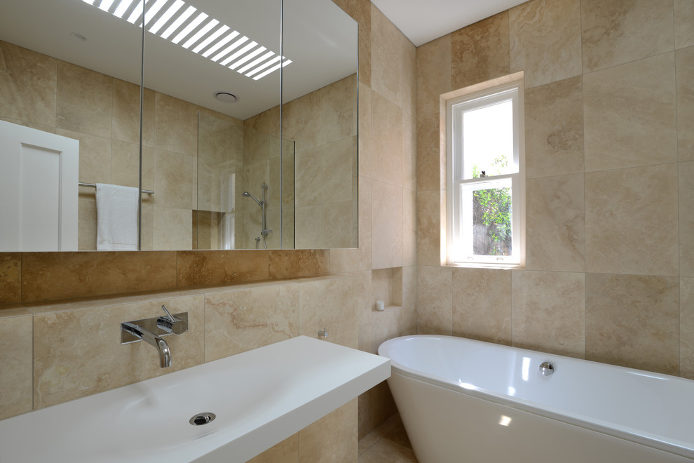Foto di una stanza da bagno minimal di medie dimensioni con vasca freestanding, piastrelle beige, lastra di pietra, pareti beige e lavabo integrato