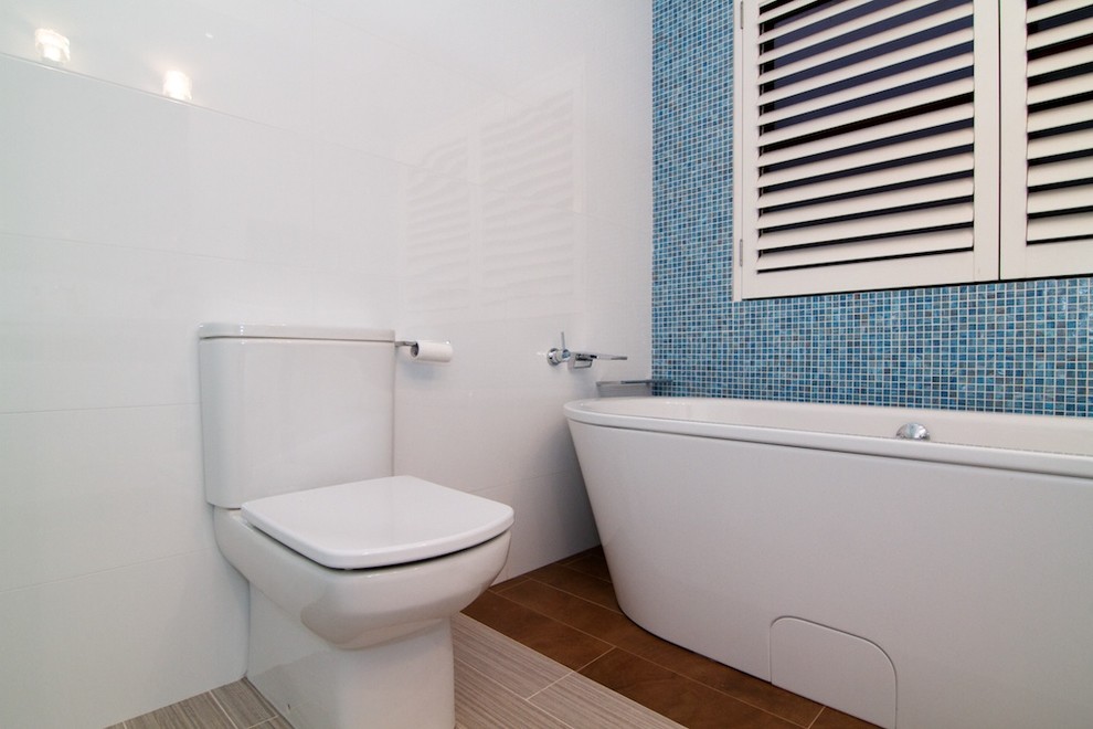 Inspiration for a medium sized modern ensuite bathroom in Sydney with flat-panel cabinets, white cabinets, solid surface worktops, a freestanding bath, a built-in shower, white tiles, porcelain tiles, white walls, ceramic flooring, a one-piece toilet, a wall-mounted sink, brown floors, a hinged door, a wall niche, double sinks and a floating vanity unit.
