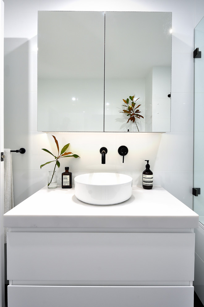 Idéer för ett litet modernt vit en-suite badrum, med luckor med glaspanel, vita skåp, ett badkar i en alkov, en öppen dusch, en toalettstol med hel cisternkåpa, vit kakel, keramikplattor, vita väggar, cementgolv, ett fristående handfat, bänkskiva i akrylsten, svart golv och med dusch som är öppen