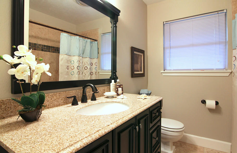 Inredning av ett amerikanskt litet badrum med dusch, med ett undermonterad handfat, svarta skåp, granitbänkskiva, ett hörnbadkar, en dusch/badkar-kombination, en toalettstol med hel cisternkåpa, beige kakel, porslinskakel, beige väggar, travertin golv och luckor med infälld panel