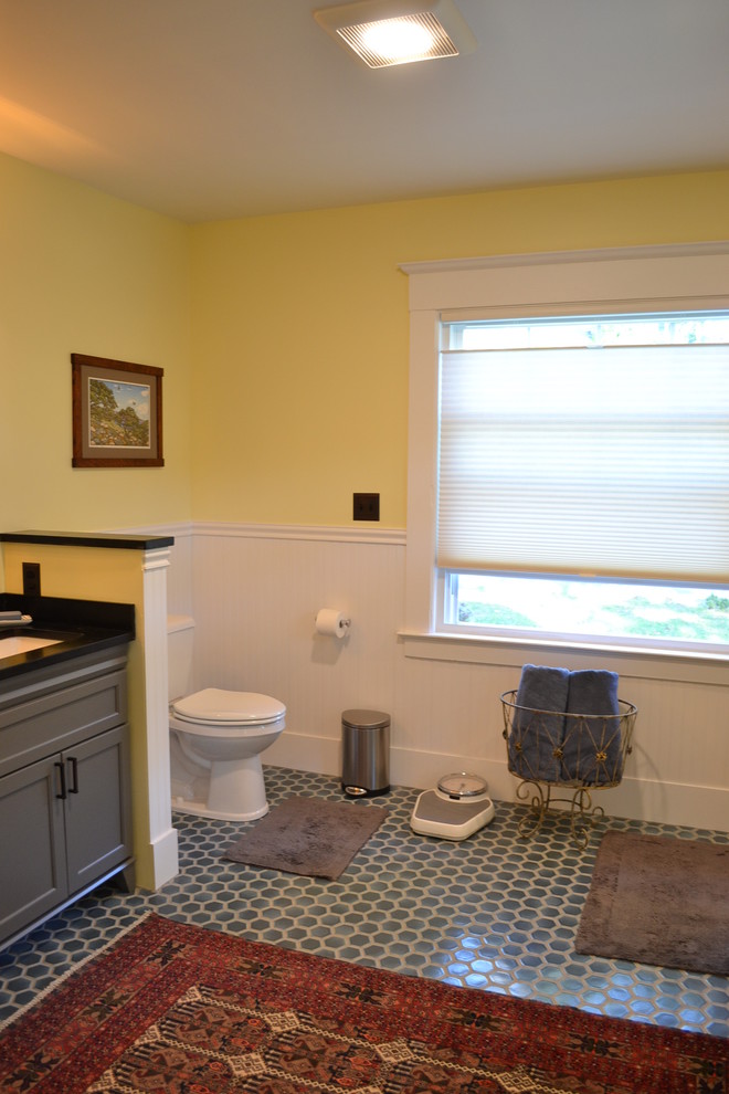 This is an example of a medium sized traditional ensuite bathroom in Boston with recessed-panel cabinets, grey cabinets, a two-piece toilet, yellow walls, ceramic flooring, a submerged sink, grey floors and black worktops.