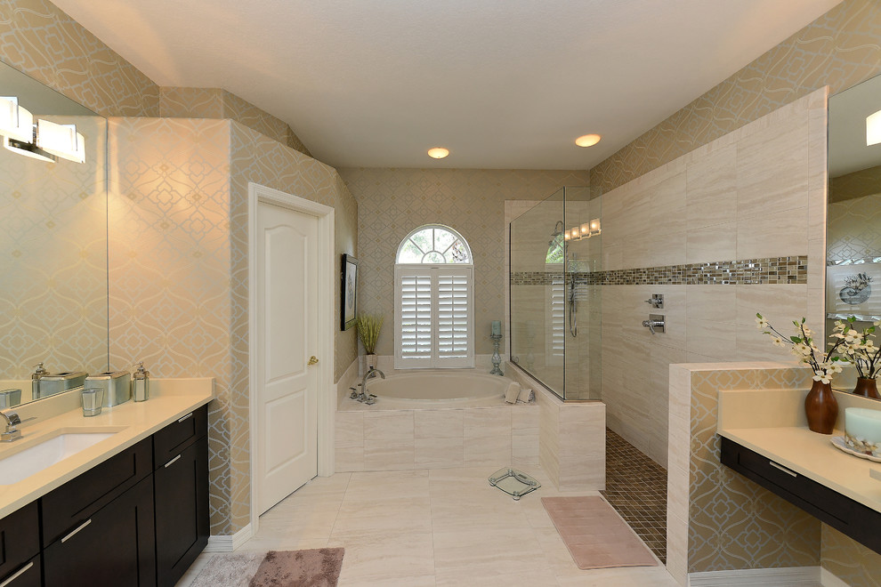 Inspiration for a large transitional master beige tile and stone slab ceramic tile bathroom remodel in Tampa with shaker cabinets, dark wood cabinets, an undermount sink, beige walls and solid surface countertops