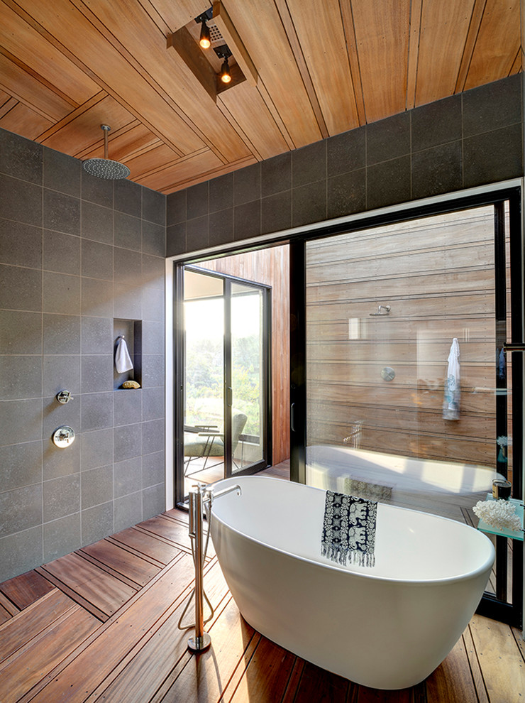 Foto de cuarto de baño minimalista con bañera exenta, ducha abierta, baldosas y/o azulejos grises, paredes grises, suelo de madera en tonos medios y ducha abierta
