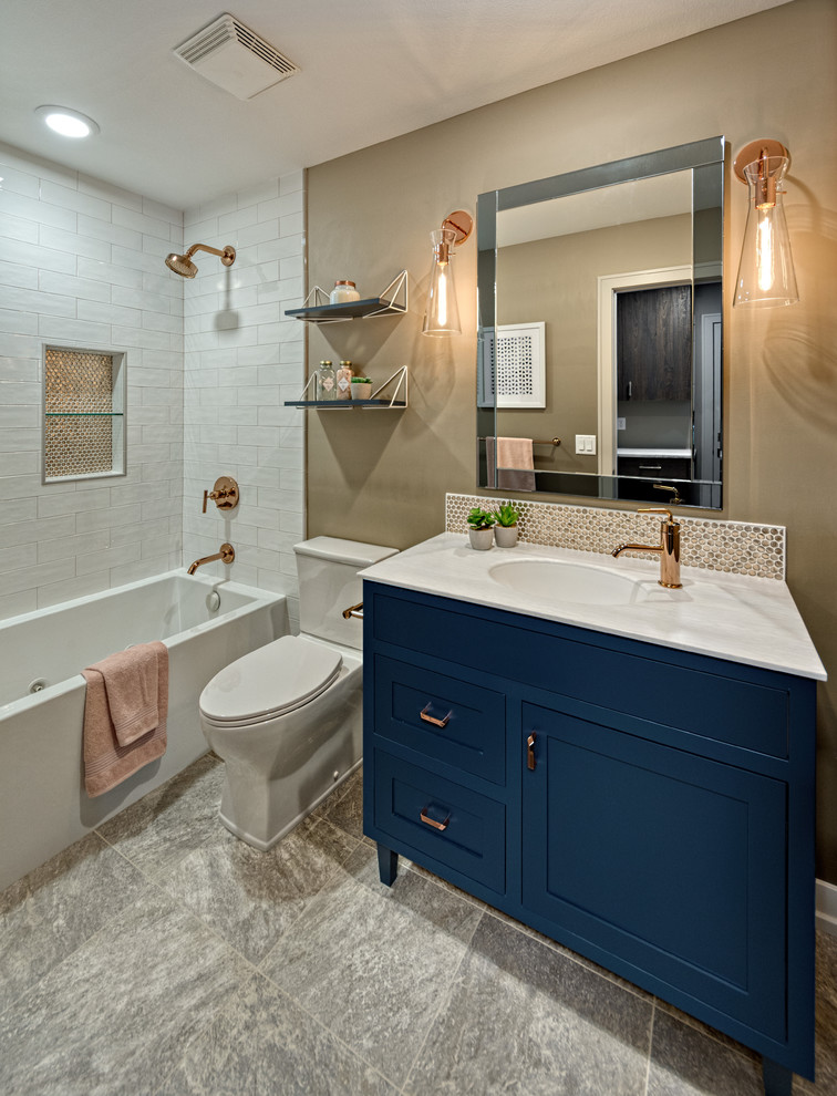 Photo of a medium sized contemporary family bathroom in Minneapolis with beaded cabinets, blue cabinets, an alcove bath, a shower/bath combination, a two-piece toilet, white tiles, ceramic tiles, beige walls, vinyl flooring, an integrated sink, solid surface worktops, grey floors, a shower curtain and grey worktops.
