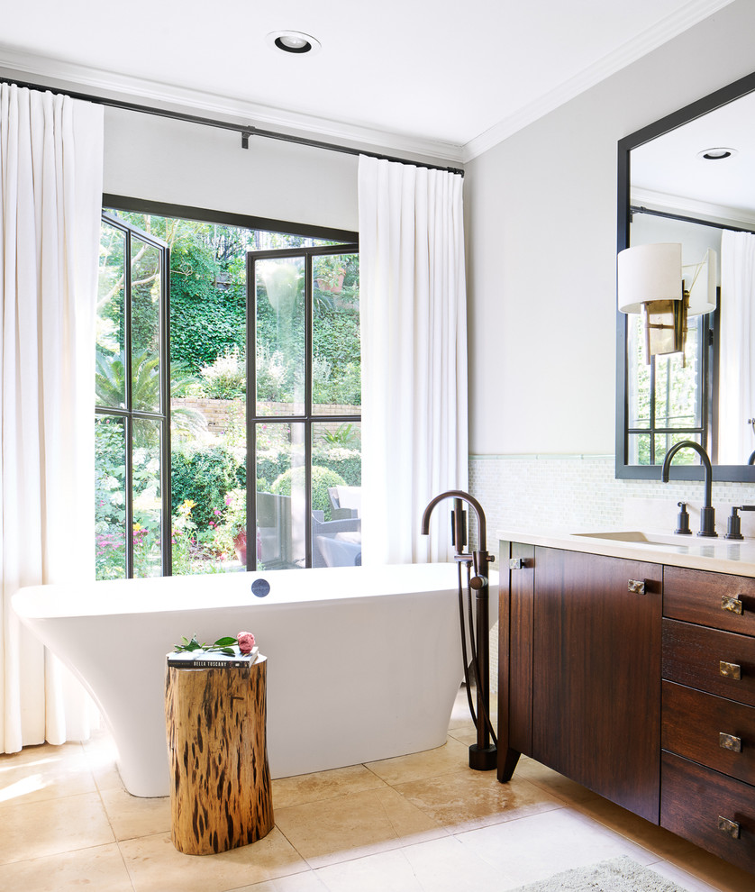Klassisk inredning av ett en-suite badrum, med skåp i mörkt trä, ett fristående badkar, en dusch i en alkov, grön kakel, glaskakel, kalkstensgolv, ett nedsänkt handfat, bänkskiva i kalksten och släta luckor