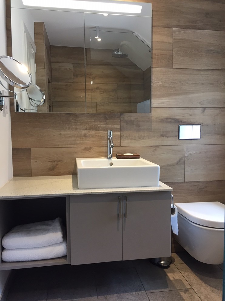 Imagen de cuarto de baño principal moderno de tamaño medio con lavabo sobreencimera, puertas de armario beige, encimera de acrílico, sanitario de pared, baldosas y/o azulejos beige y suelo de baldosas de porcelana