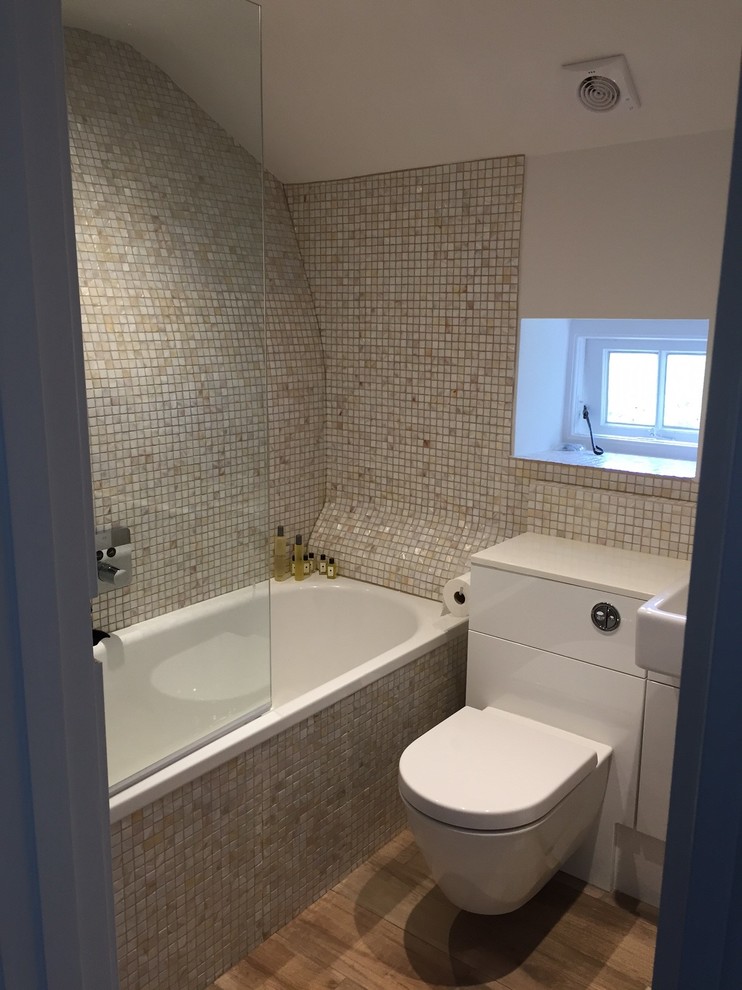 Inspiration for a modern family bathroom in Dorset with white cabinets, an alcove bath, a wall mounted toilet, multi-coloured tiles, white walls and porcelain flooring.