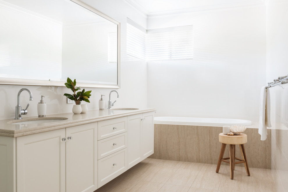 Foto på ett stort vintage beige badrum med dusch, med luckor med infälld panel, vita skåp, ett platsbyggt badkar, vit kakel, vita väggar, ett undermonterad handfat och beiget golv