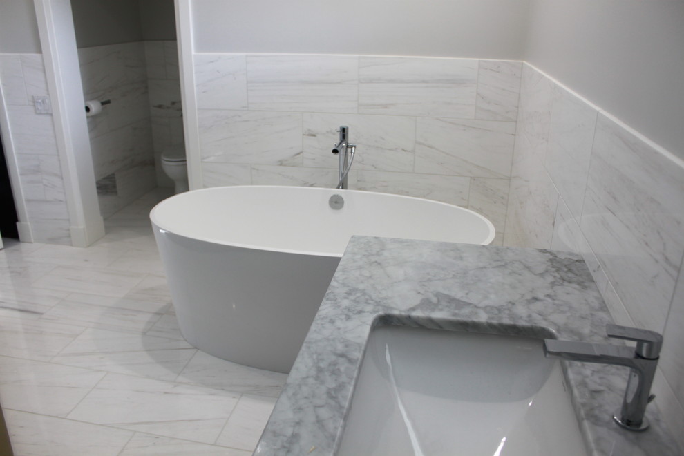 Ispirazione per una grande stanza da bagno minimal con vasca freestanding, WC monopezzo, piastrelle grigie, piastrelle in pietra, pareti grigie, pavimento in marmo, lavabo sottopiano e top in marmo