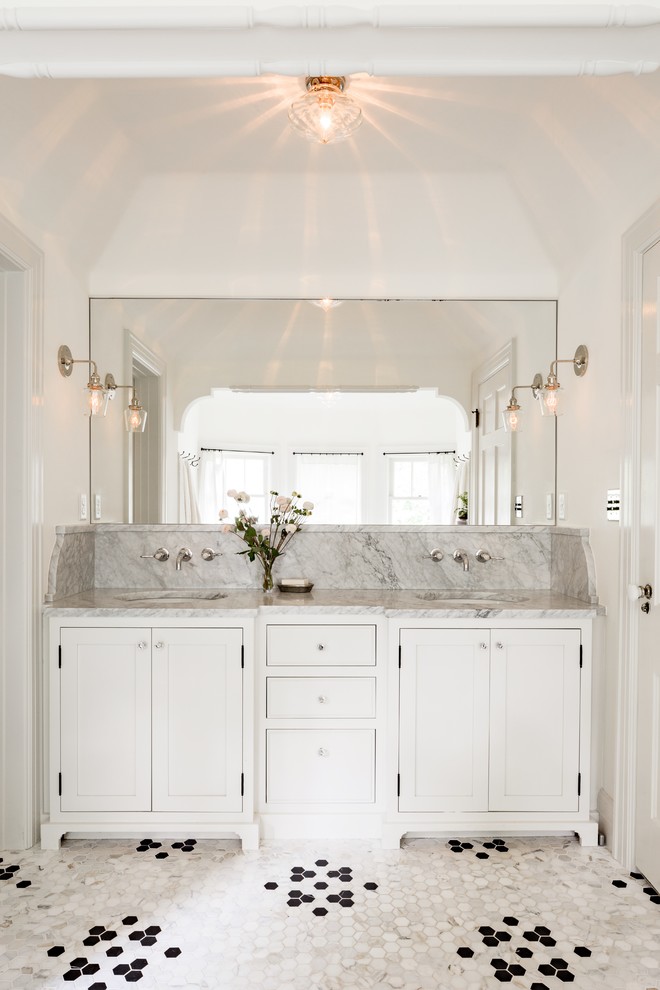 Imagen de cuarto de baño tradicional con lavabo bajoencimera, armarios estilo shaker, puertas de armario blancas, paredes blancas, suelo con mosaicos de baldosas y espejo con luz