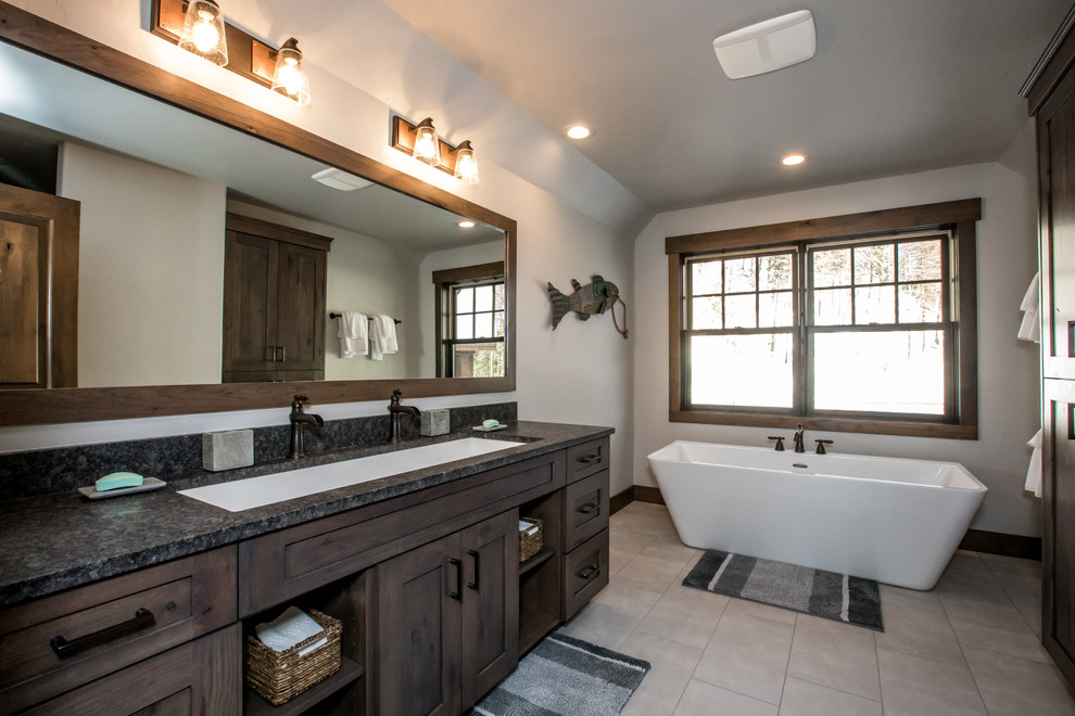 Réalisation d'une salle de bain chalet en bois foncé avec un placard à porte shaker, une baignoire indépendante, un mur blanc, un sol en carrelage de porcelaine, une grande vasque, un plan de toilette en granite, un sol beige et un plan de toilette gris.