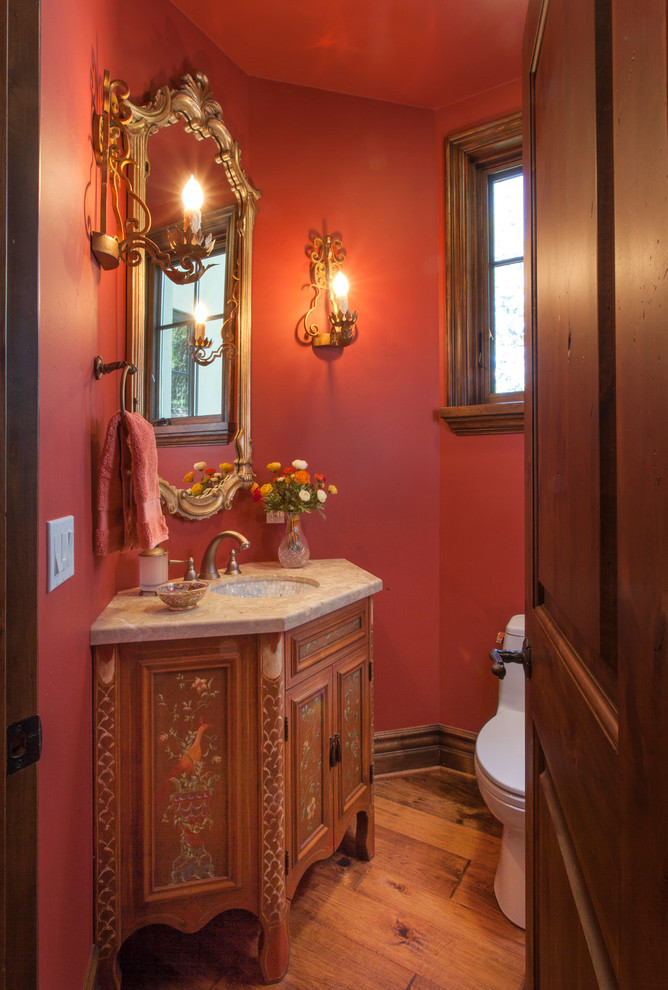 Example of a small classic medium tone wood floor powder room design in Los Angeles with recessed-panel cabinets, medium tone wood cabinets, a one-piece toilet, red walls, an undermount sink and marble countertops