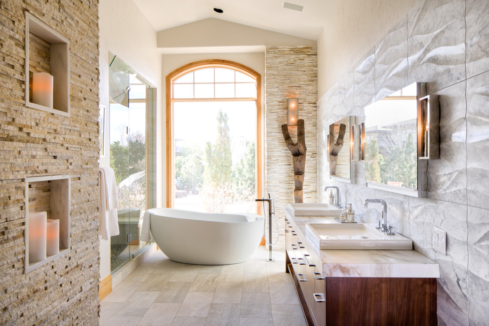 Modern inredning av ett en-suite badrum, med ett fristående handfat, släta luckor, skåp i mellenmörkt trä, ett fristående badkar, en dusch i en alkov, grå kakel, beige väggar, marmorbänkskiva, stenkakel och klinkergolv i keramik