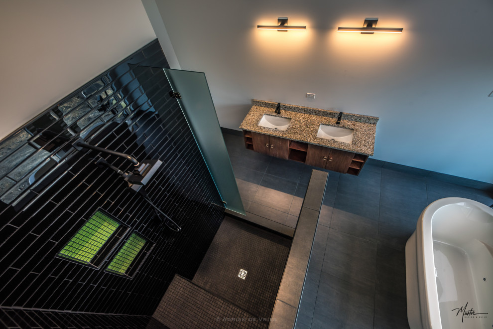 Bild på ett mellanstort industriellt en-suite badrum, med släta luckor, skåp i mörkt trä, ett fristående badkar, en hörndusch, svart kakel, tunnelbanekakel, grå väggar, betonggolv, ett undermonterad handfat, granitbänkskiva, svart golv och dusch med gångjärnsdörr